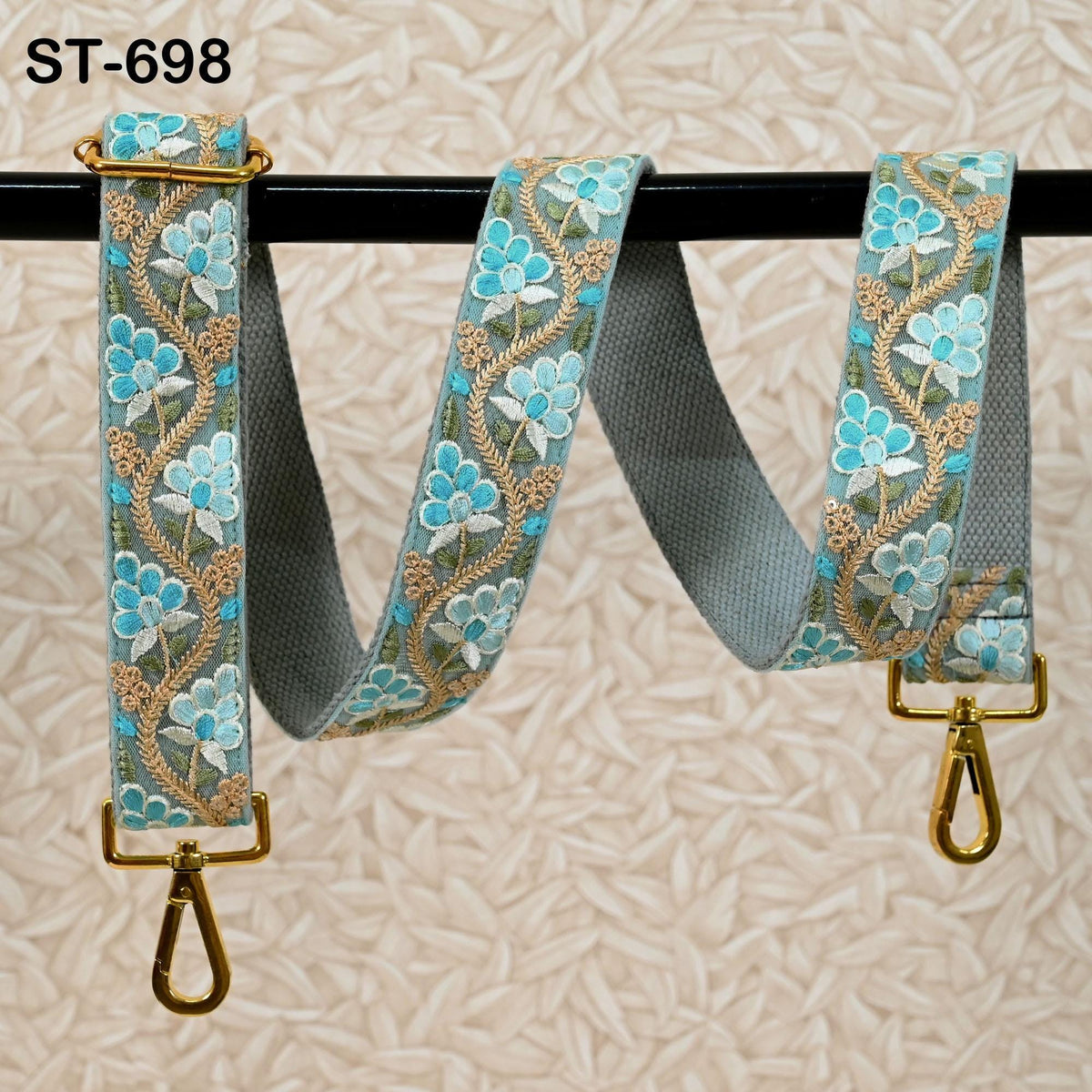A floral-patterned fabric strap with gold metal hooks attached, hanging on a black rod.