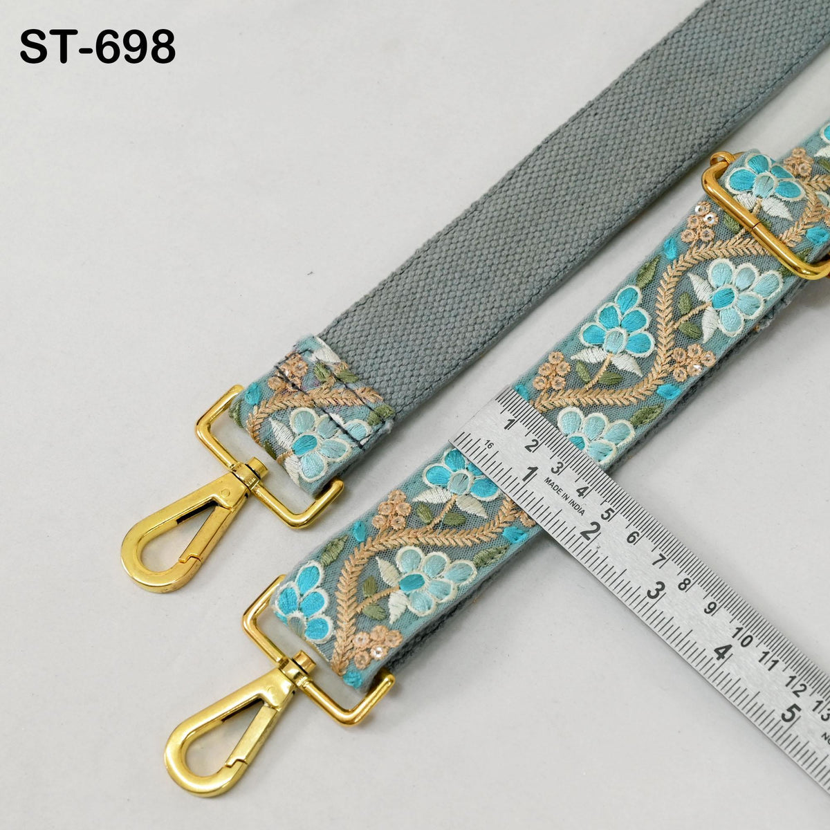 a gray strap with a floral pattern and two gold metal hooks, placed next to a ruler for size comparison.