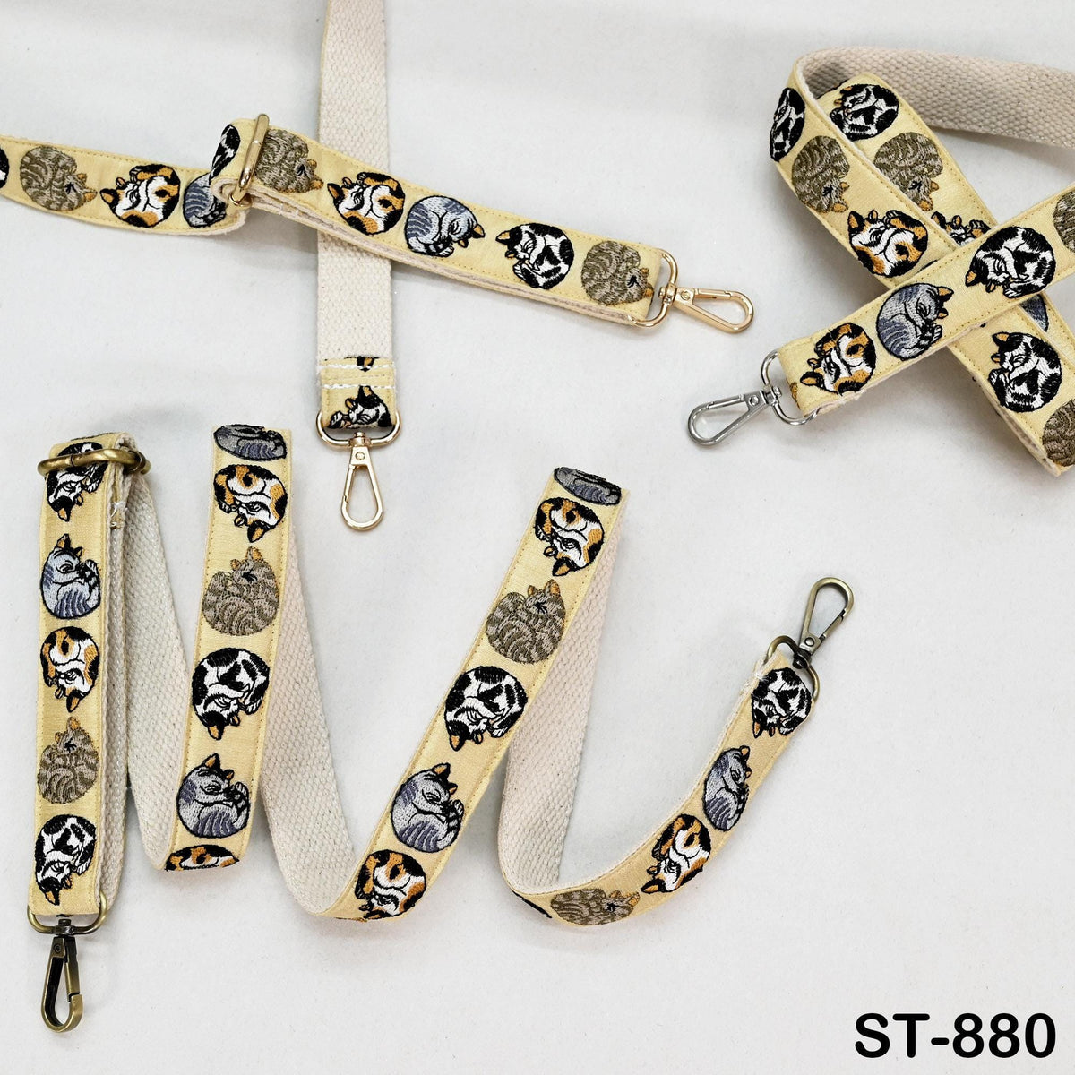 a collection of beige and white straps adorned with black and orange cat designs, including a cat-themed bag strap and a cat-themed keychain strap.