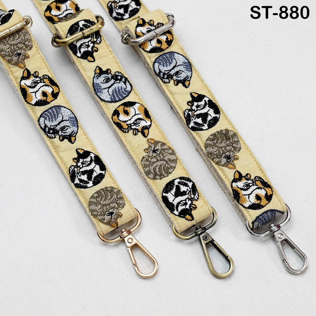 a collection of three beige straps with cat designs, each featuring a metal clasp and a metal hook.