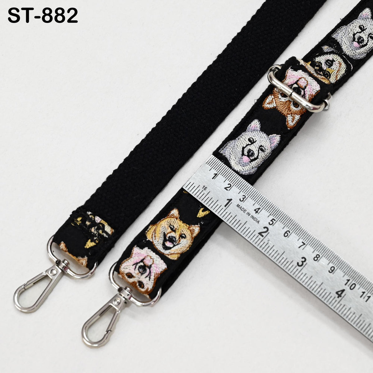a black strap with a repeating pattern of dog faces on it, and a ruler is placed next to it, indicating the strap's length.