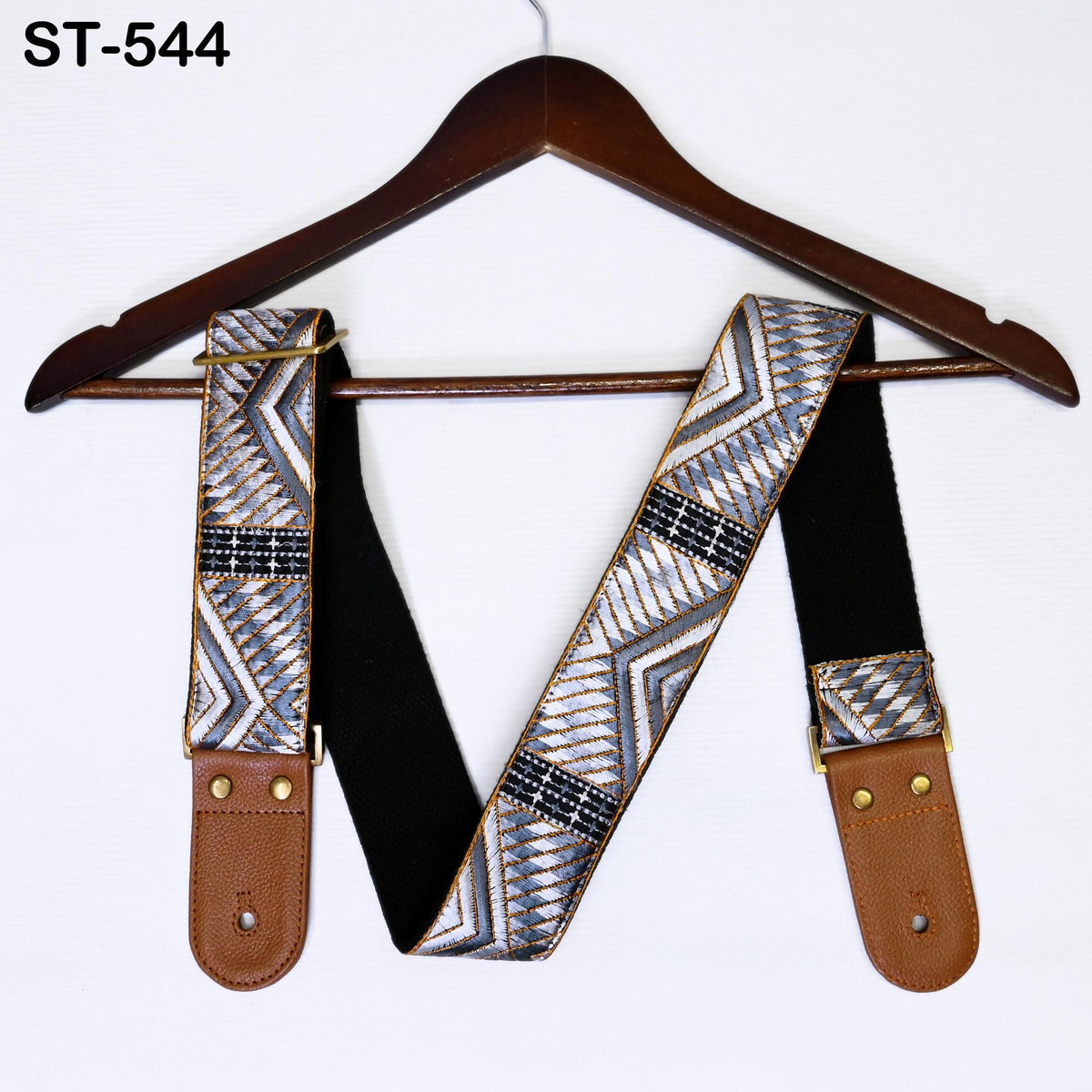 A brown wooden hanger with a patterned guitar strap hanging on it.