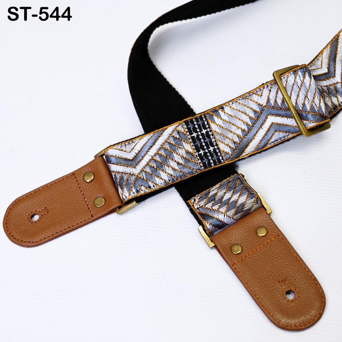 A close-up image of a brown leather guitar strap with a patterned design, featuring a black strap and brass hardware.