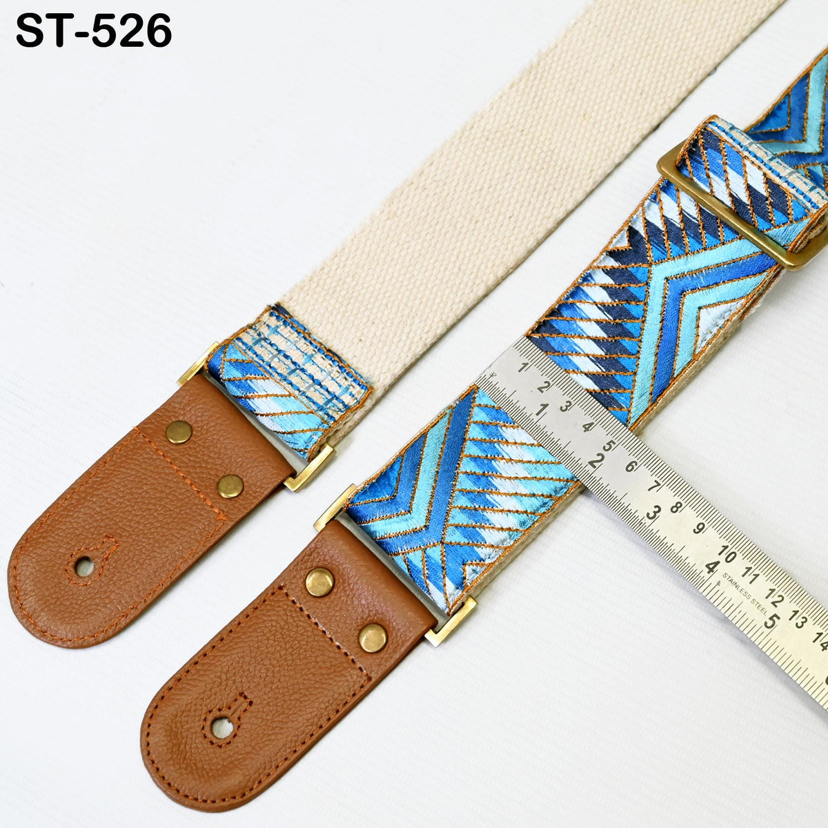 a beige guitar strap with a patterned design, placed on a white surface next to a ruler for size comparison.