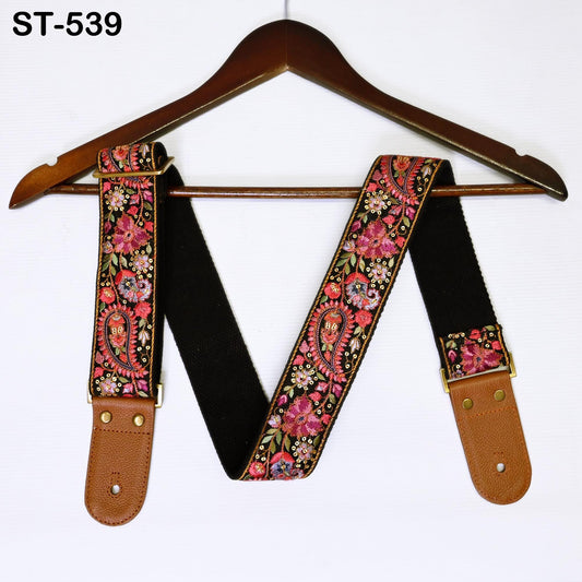 A decorative guitar strap with a floral pattern is hanging on a wooden hanger.