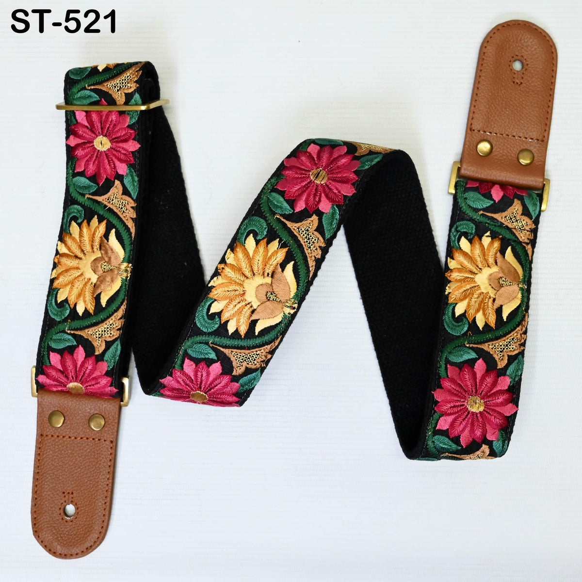A colorful guitar strap with floral patterns in shades of pink, yellow, and green. The strap is made of black material and has a brown leather buckle.