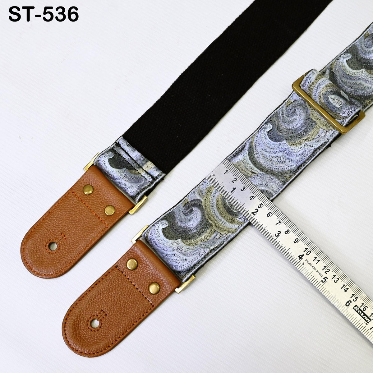 a guitar strap with a black and gray floral pattern, and a ruler placed next to it on a white background.