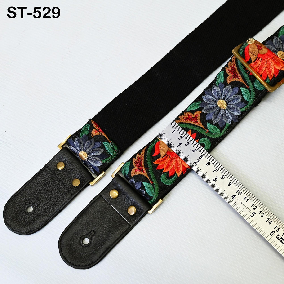 A black guitar strap with a floral pattern and a ruler placed next to it.