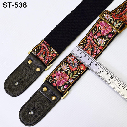 A black guitar strap with a floral pattern and a ruler placed next to it, indicating the strap's length.