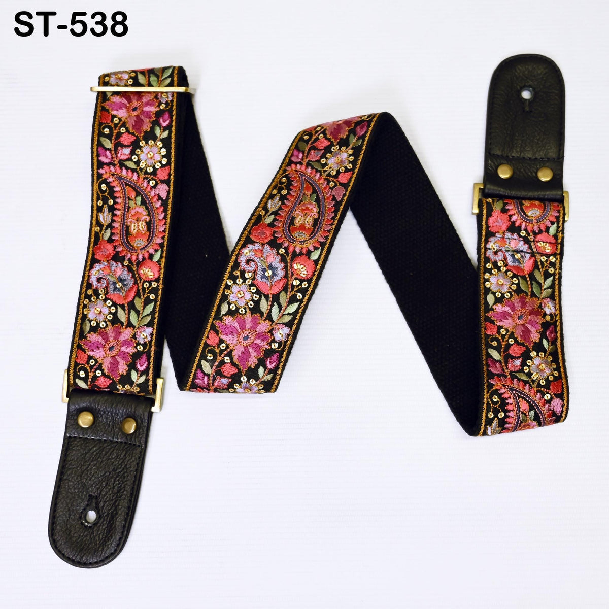 A colorful guitar strap with a paisley pattern and a black leather buckle.