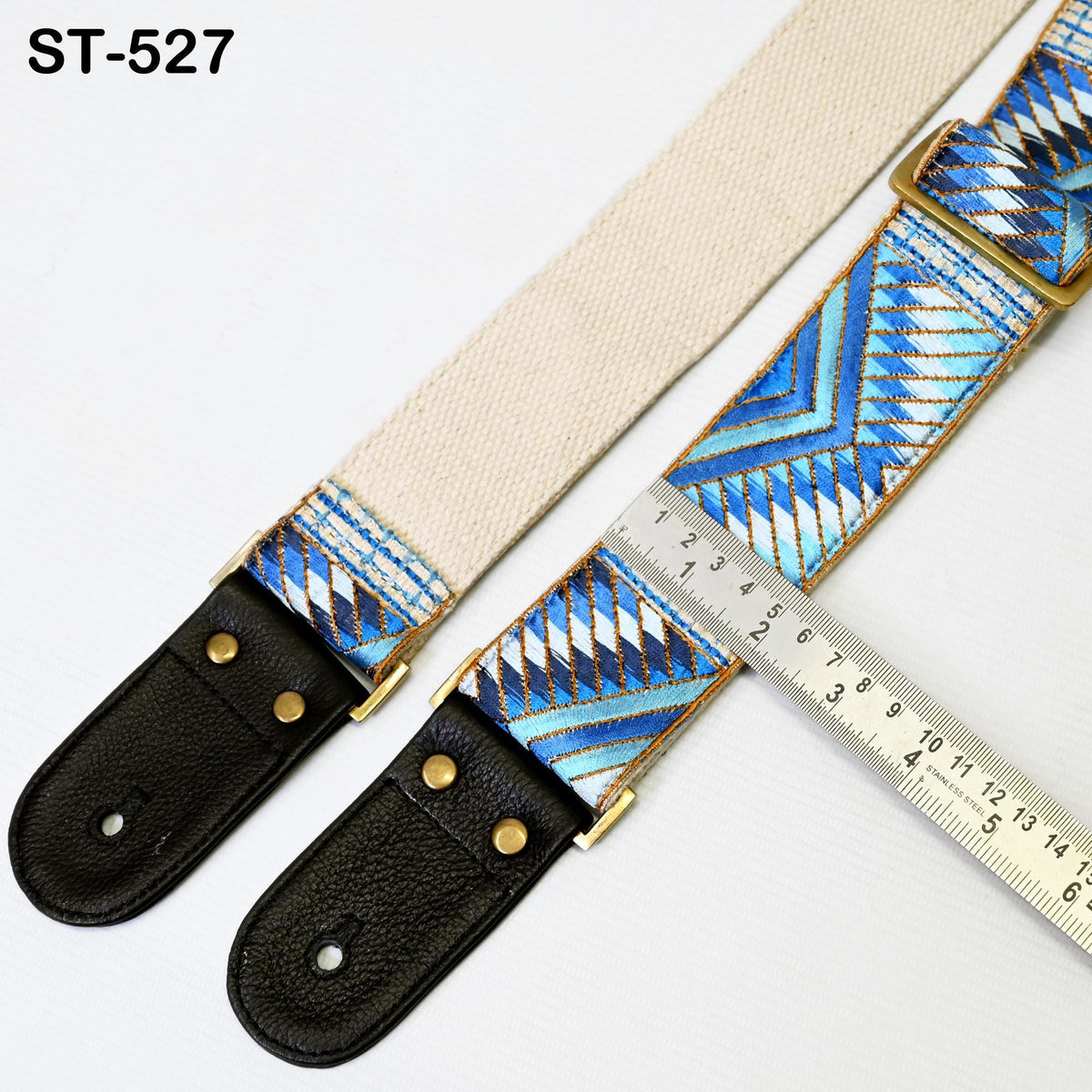 A beige and blue patterned guitar strap with a black leather buckle, and a ruler placed next to it, indicating the strap's length.