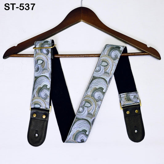 A pair of guitar suspenders with a patterned fabric design hanging on a wooden hanger.
