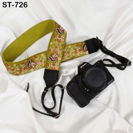 A green and red floral patterned camera strap and a black Nikon camera are placed on a white surface.