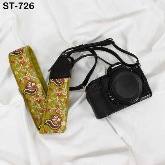 A black camera with a green floral patterned strap is placed on a white surface.