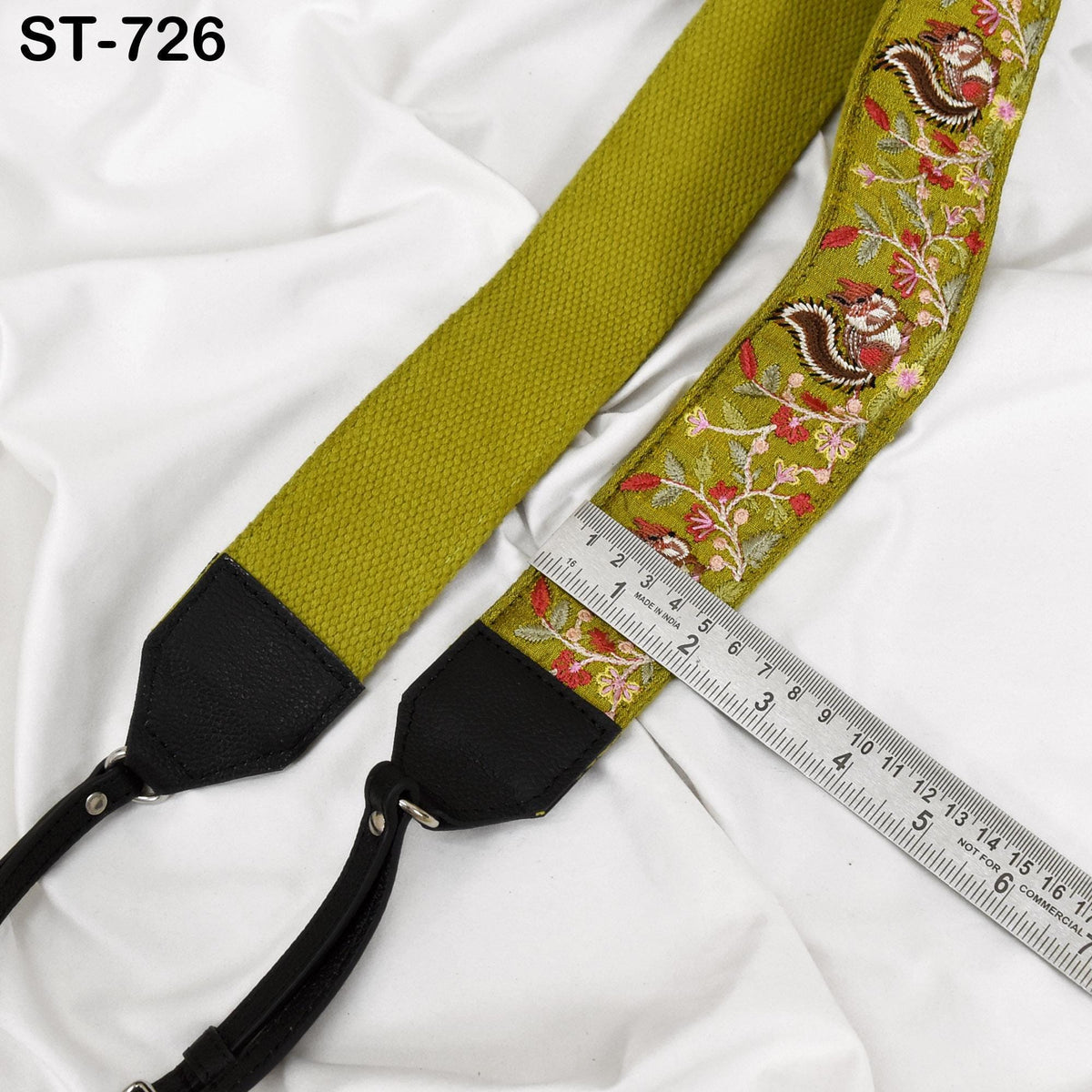 A green and black camera strap with a floral pattern, resting on a white surface. A ruler is placed next to the strap, indicating its length.