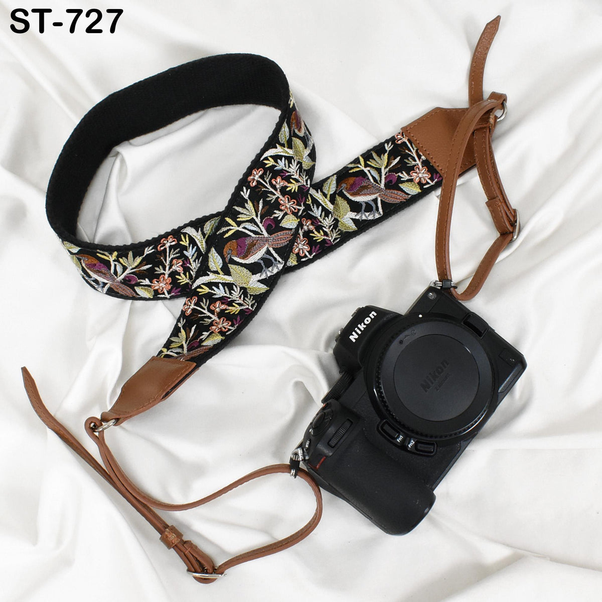 A floral patterned camera strap and a black Nikon camera with a lens cap are placed on a white surface.