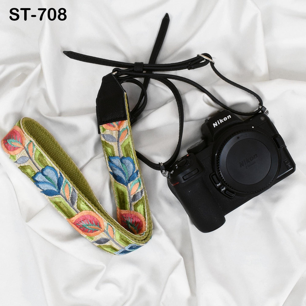 A black camera with a colorful floral patterned strap is placed on a white surface.