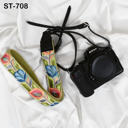 A black camera with a colorful floral patterned strap is placed on a white surface.