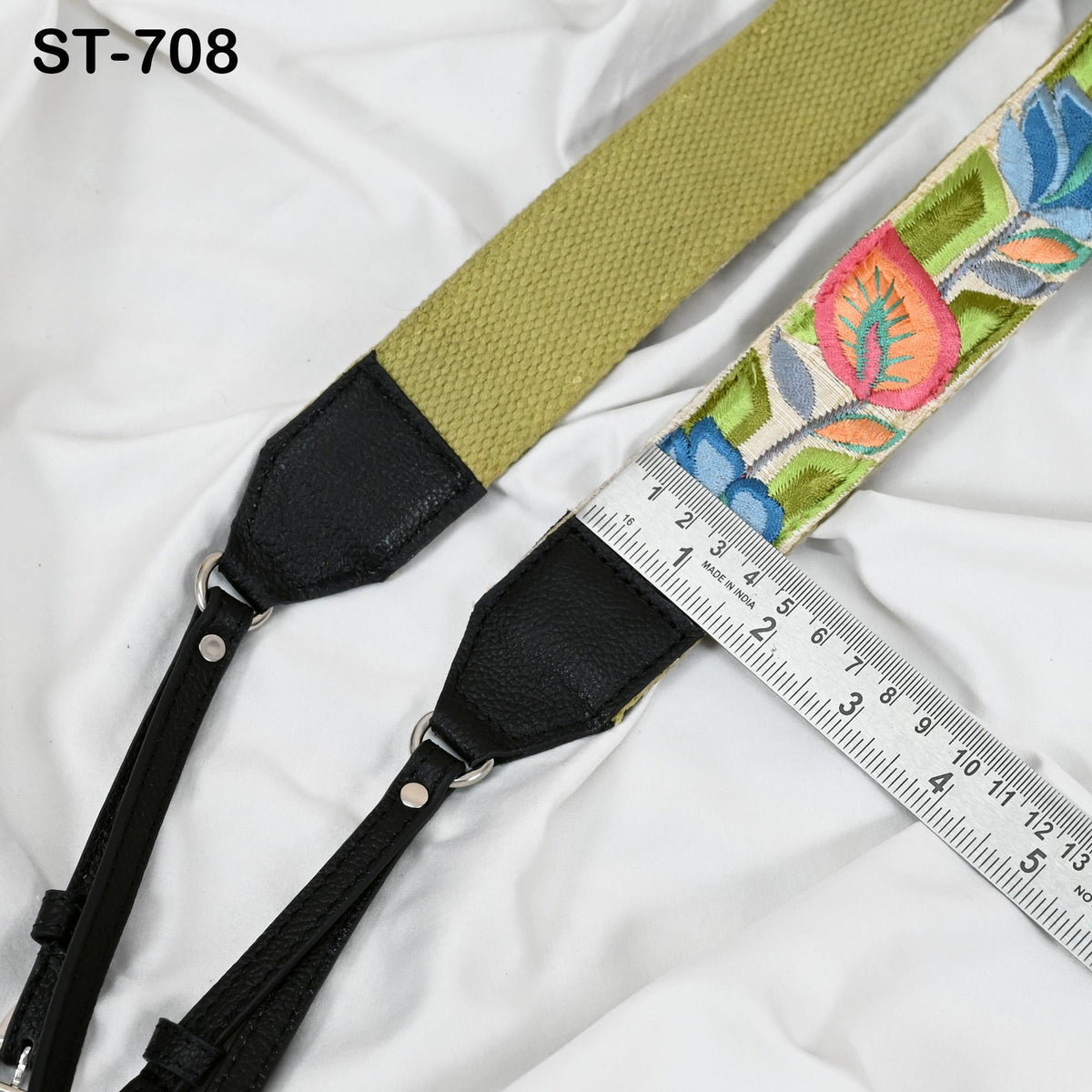 A colorful floral patterned strap with a black leather attachment and a ruler for size comparison.