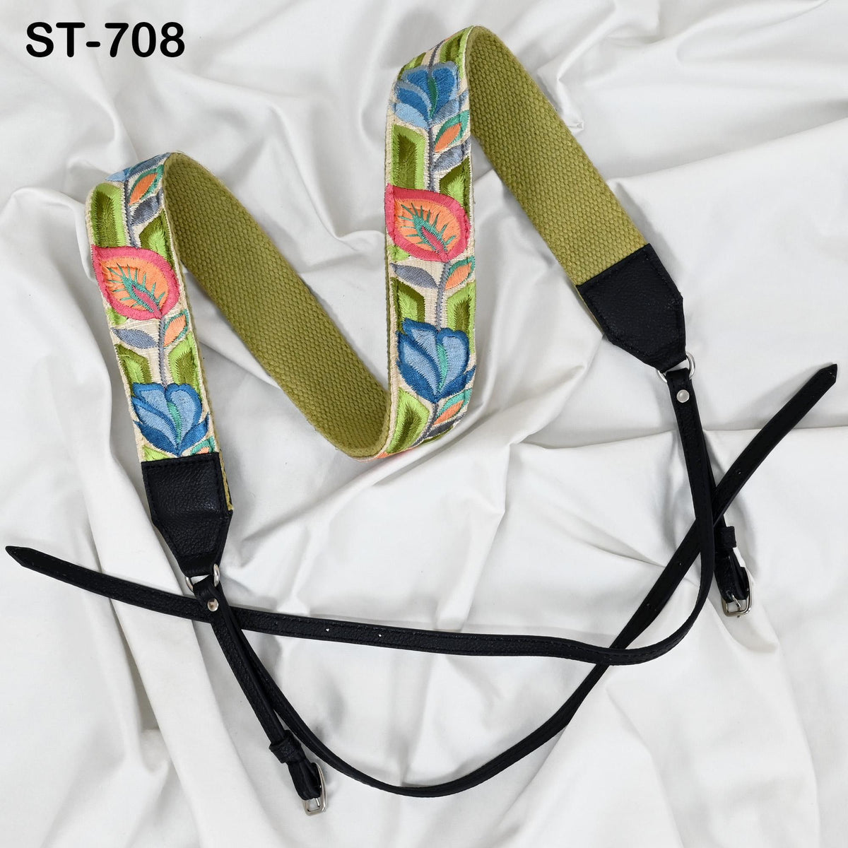 A colorful, patterned camera strap with a floral design, placed on a white fabric surface.
