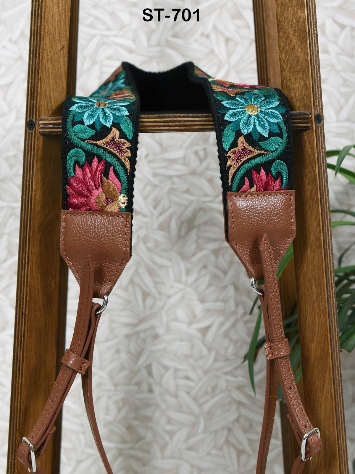 A brown leather strap with a floral embroidered pattern, hanging on a wooden stand.