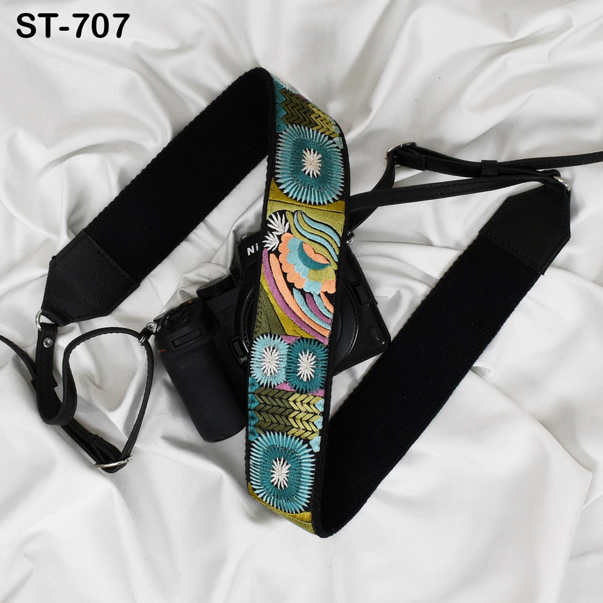 A camera strap with a colorful, floral pattern is draped over a camera, along with a lens cap and a black strap.
