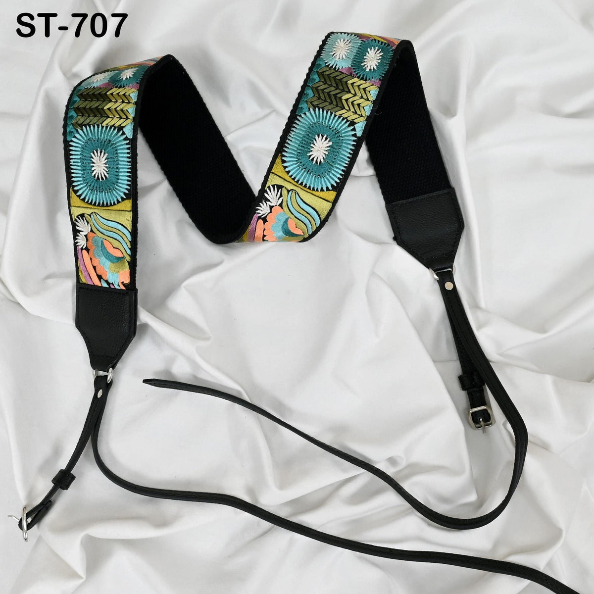 A colorful patterned strap with a black leather buckle, laid out on a white fabric surface.
