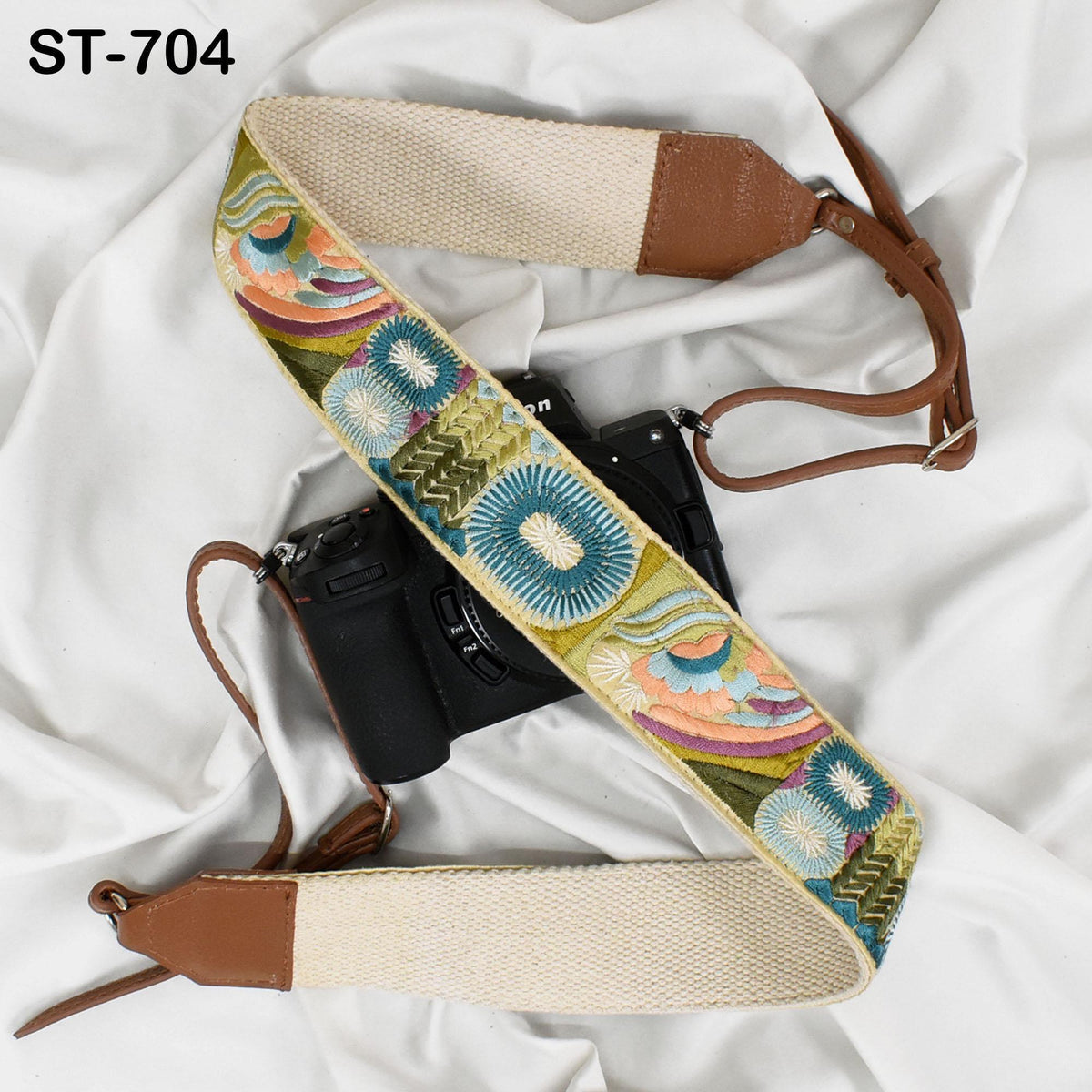 a camera strap with a colorful, embroidered pattern, placed on a white fabric surface.
