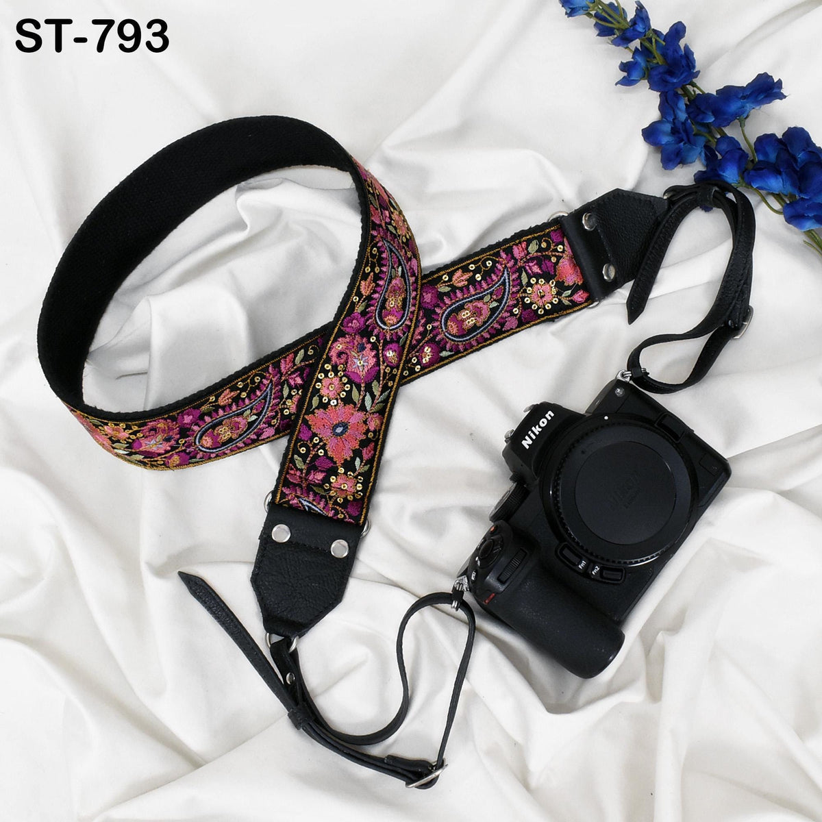 A floral patterned camera strap and a Nikon camera are placed on a white fabric surface.