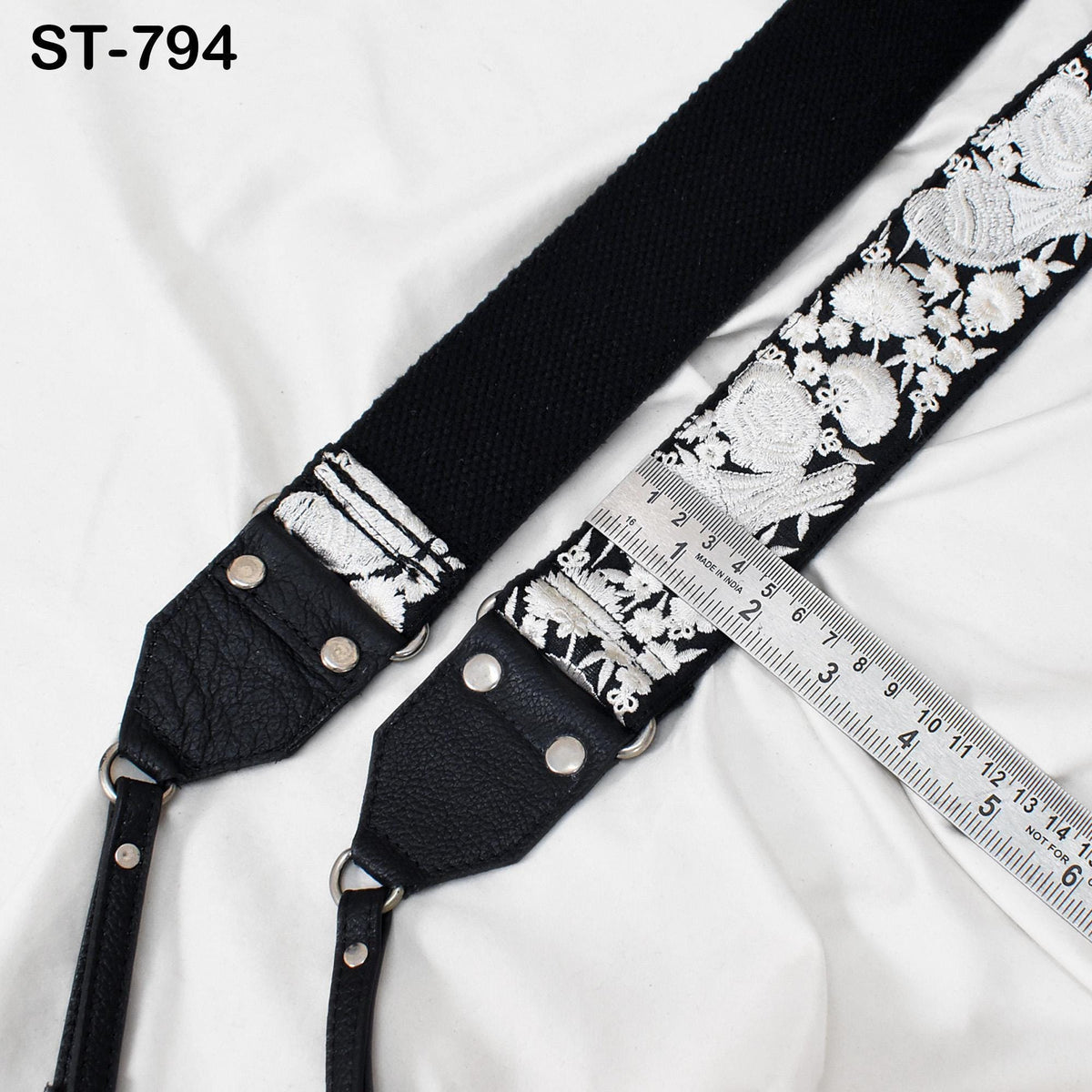 a black and white strap with a floral pattern, resting on a white surface. There is a ruler placed next to the strap, indicating its size or length.