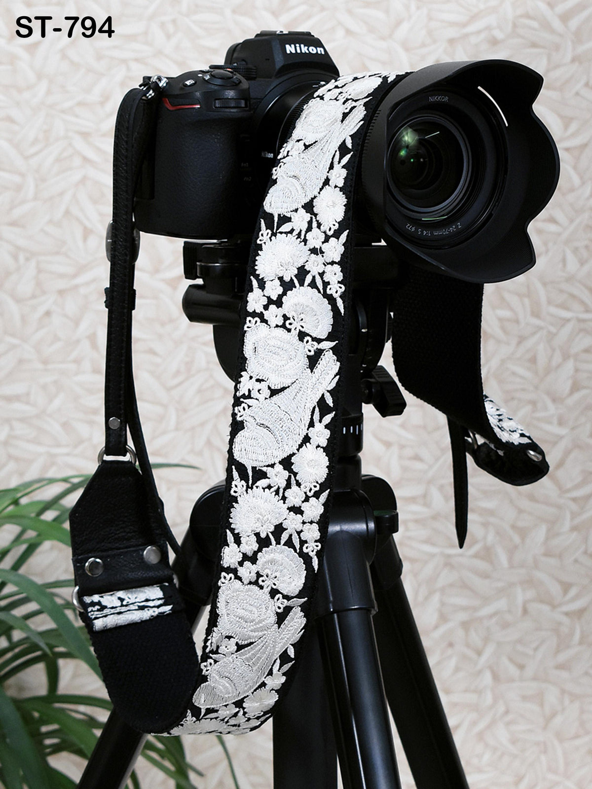 A black and white patterned camera strap is attached to a tripod, with a Nikon camera body visible in the background.