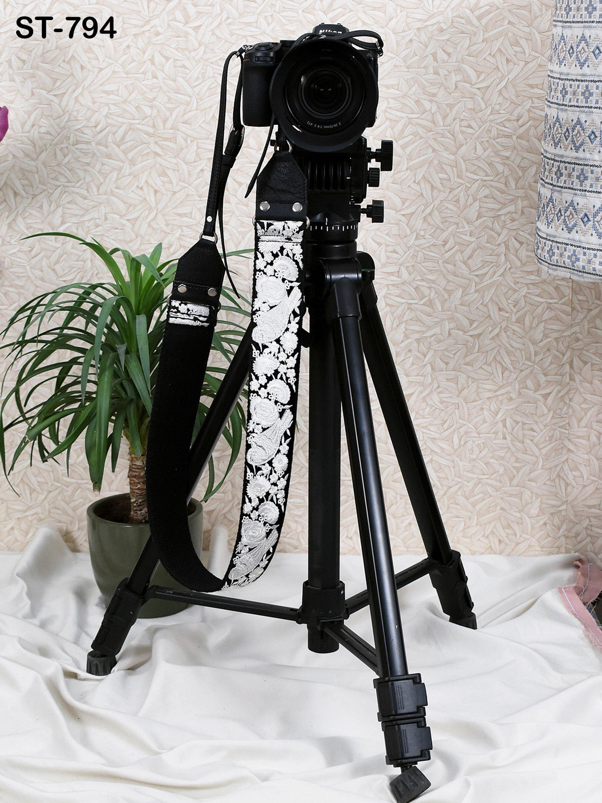 A black tripod with a camera attached to it, standing on a white cloth.