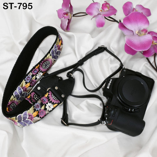 A floral patterned camera strap and a Nikon camera are placed on a white surface, with pink orchids in the background.