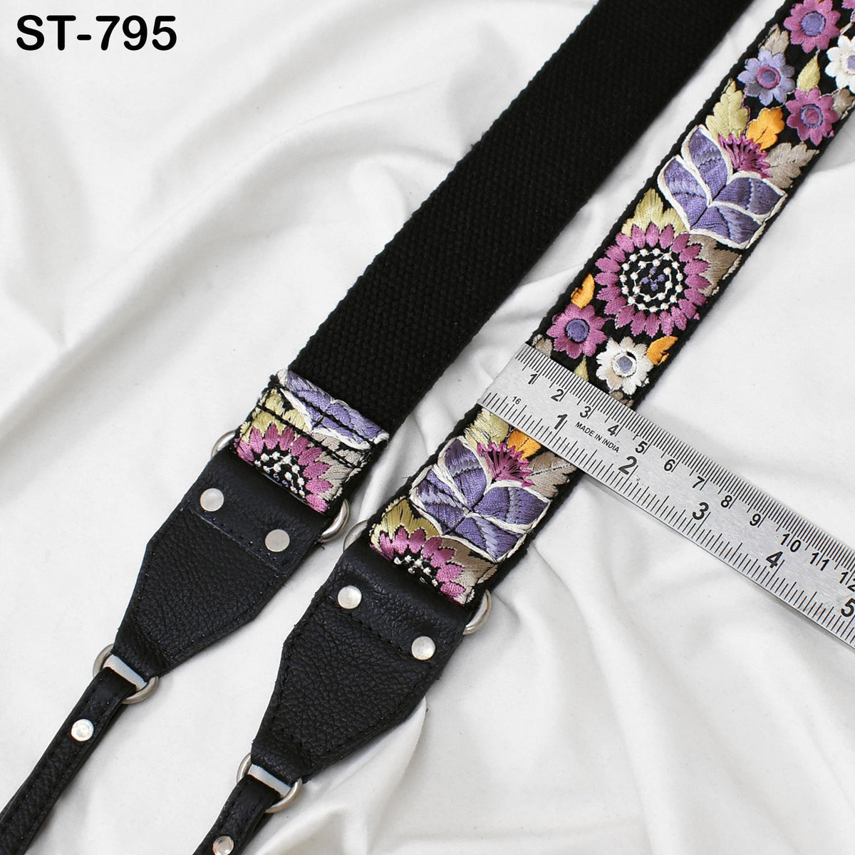 A black camera strap with a floral pattern and a ruler placed on top of it.