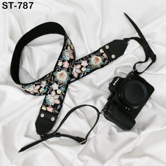 A floral patterned camera strap and a black camera with a lens attached are placed on a white fabric surface.