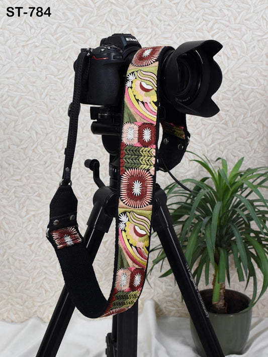 A black camera with a colorful patterned strap is placed on a tripod, with a potted plant in the background.