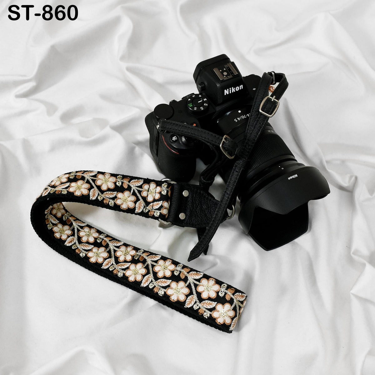 A black and white floral camera strap is draped over a black Nikon camera, with the strap's pattern visible.
