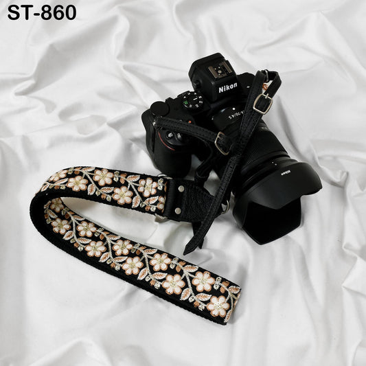 A black and white floral camera strap is draped over a black Nikon camera, with the strap's pattern visible.