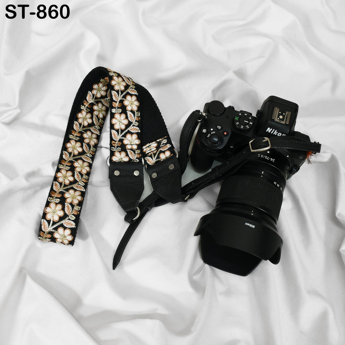 A black camera with a floral patterned strap and a lens attached to it, placed on a white surface.