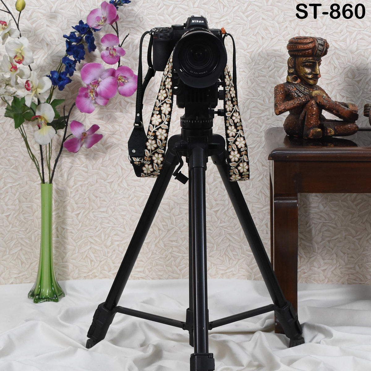 A tripod with a camera attached to it, along with a decorative statue and a vase of flowers, is displayed in the image.
