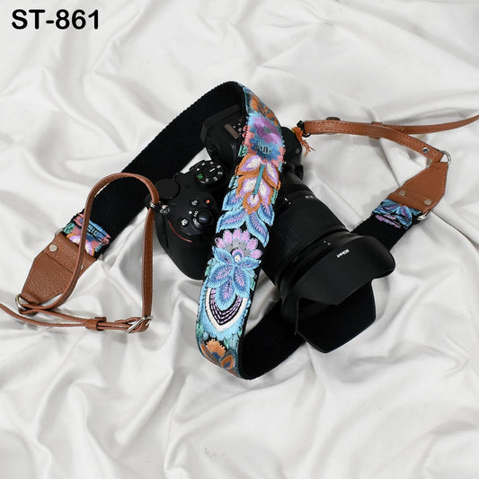 A camera with a colorful floral patterned strap is placed on a white surface.