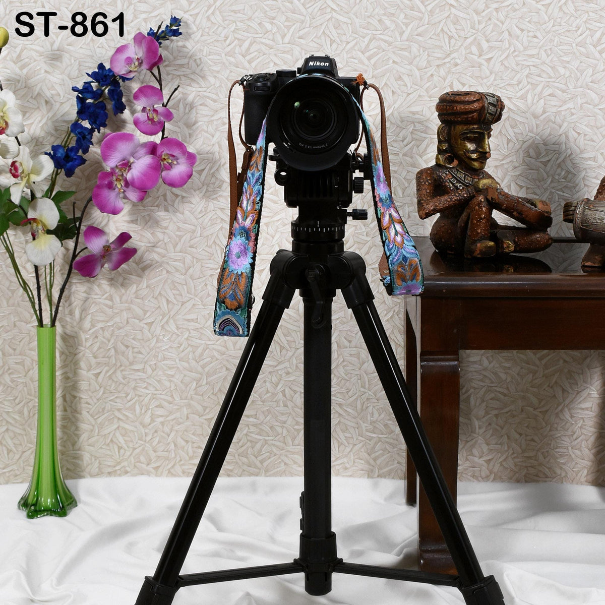 a tripod with a camera attached to it, placed on a table next to a vase of flowers and a figurine.