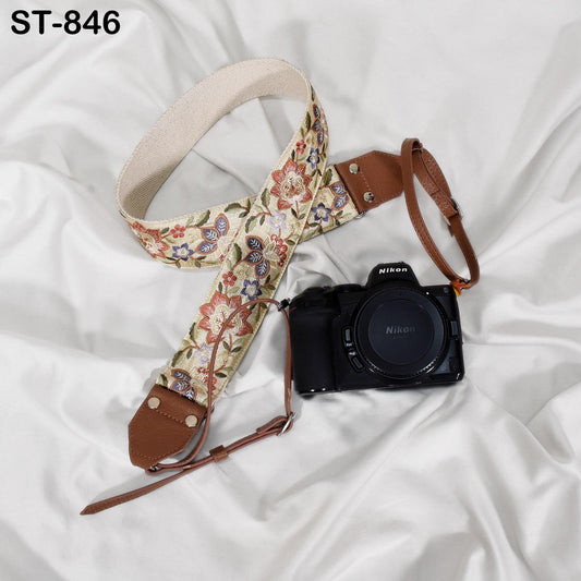 A floral patterned camera strap and a black Nikon camera are placed on a white fabric surface.