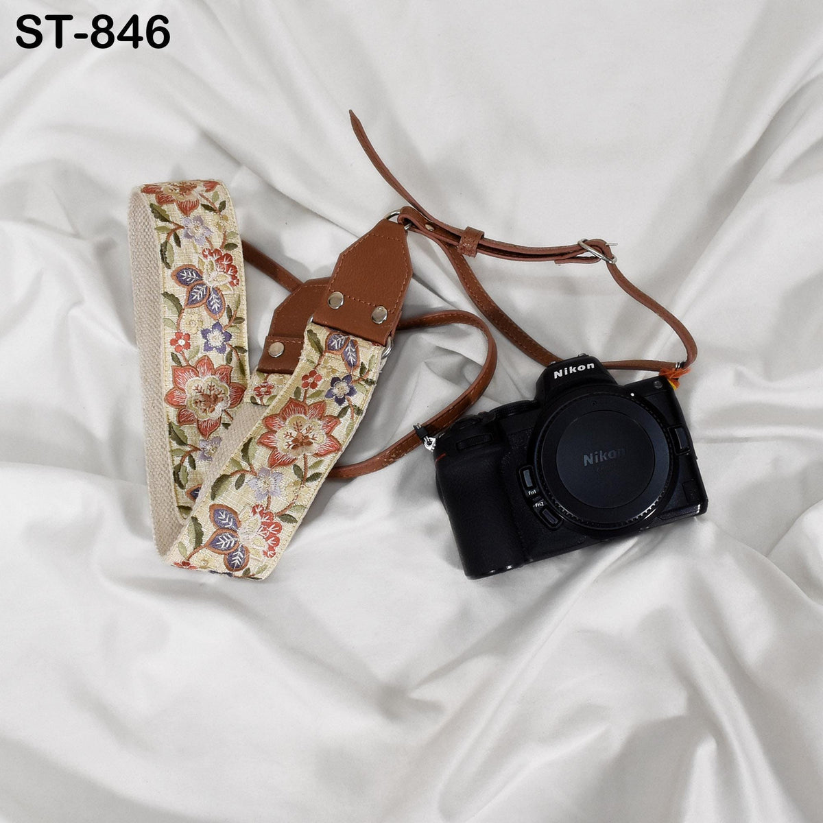 A floral patterned camera strap and a black Nikon camera are placed on a white fabric surface.