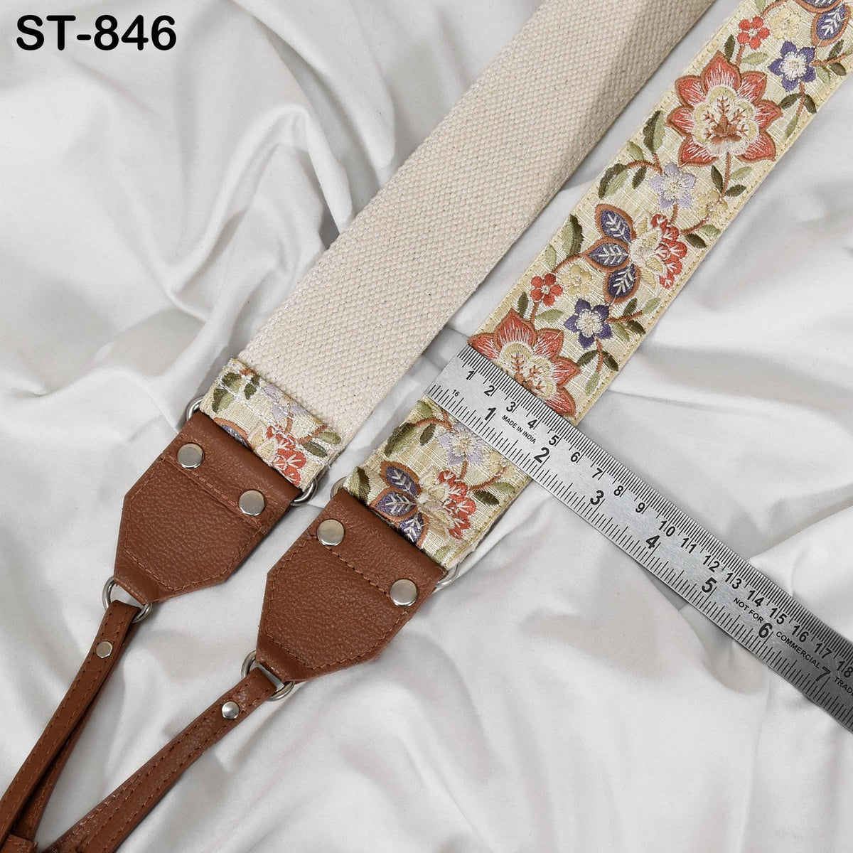 A beige strap with a floral pattern is placed on a white fabric surface, with a ruler placed next to it.