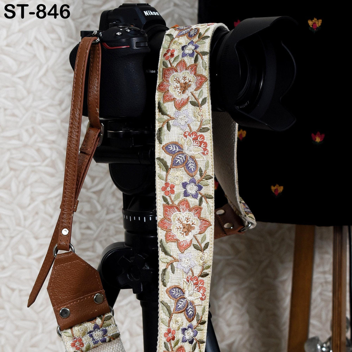 A black camera with a floral patterned strap hanging from it, placed on a tripod against a white background.
