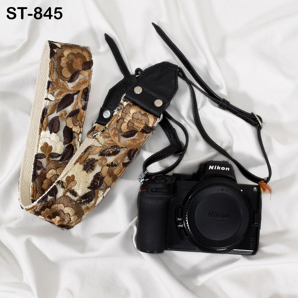 A black and brown floral camera strap and a black Nikon camera are placed on a white surface.