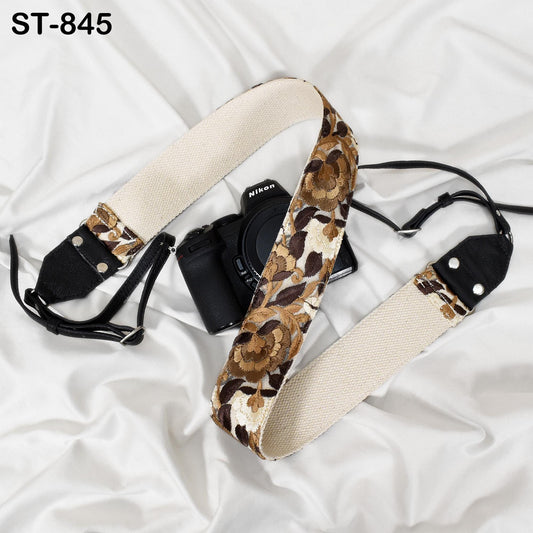 A black and white floral patterned camera strap is draped over a black camera body, with the strap's strap hanging off the edge of the camera.