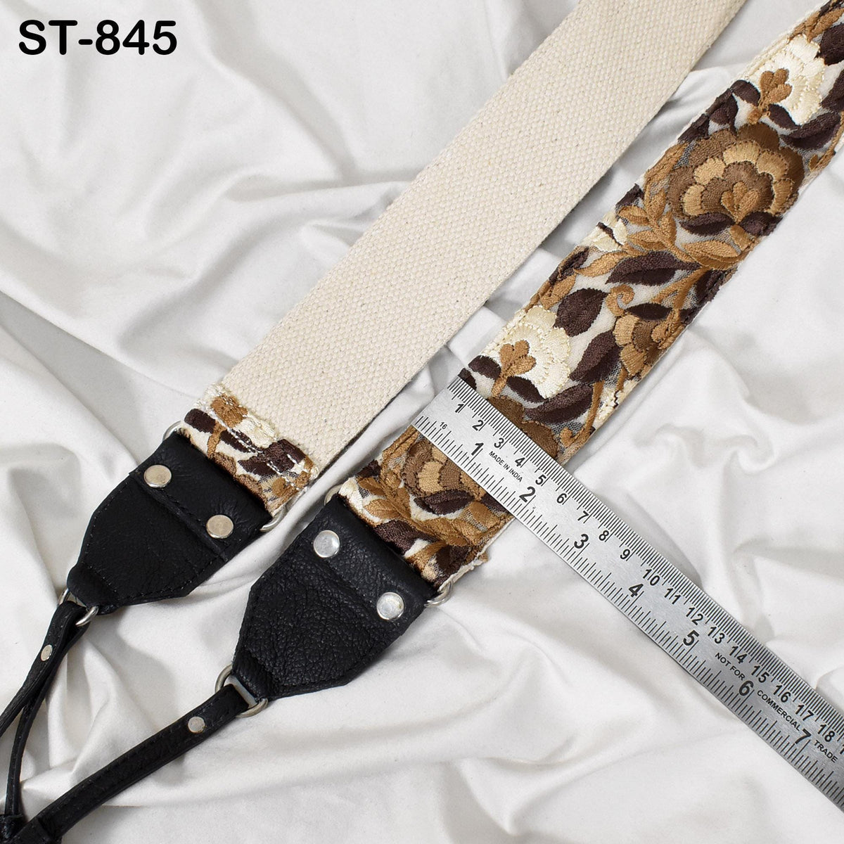 a beige and brown floral patterned strap with a black leather attachment, placed on a white fabric surface. A ruler is visible next to the strap, indicating its size or length.