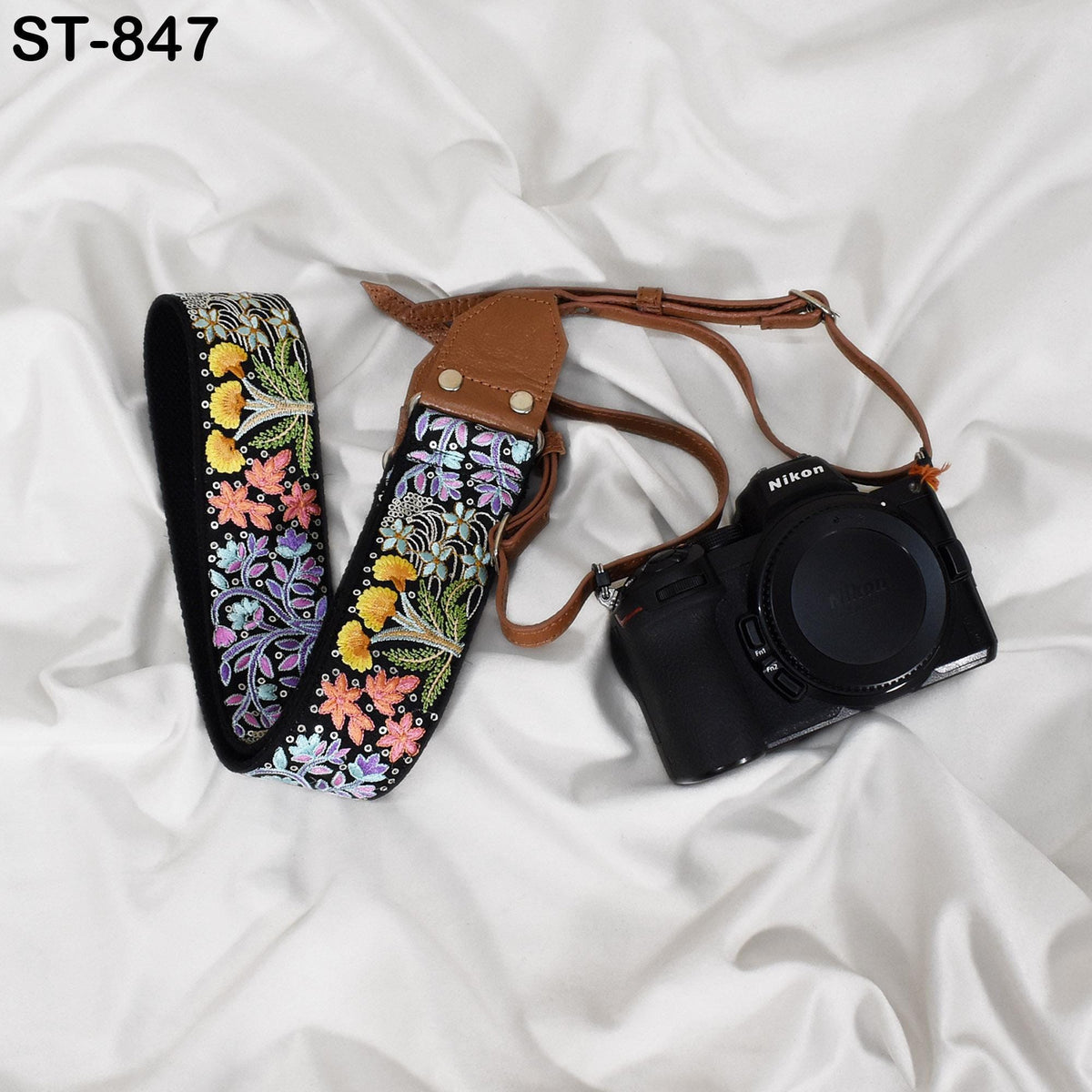A floral patterned camera strap and a black Nikon camera are placed on a white fabric surface.